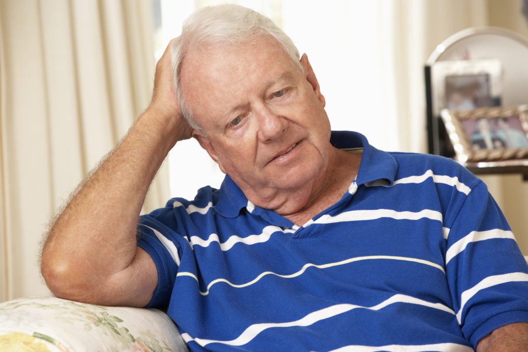 Unhappy Retired Senior Man Sitting On Sofa At Home