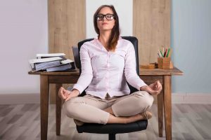 Young Businesswoman Sitting On Chair Meditating In Office